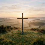 Wooden cross silhouetted against sunrise over misty rolling countryside